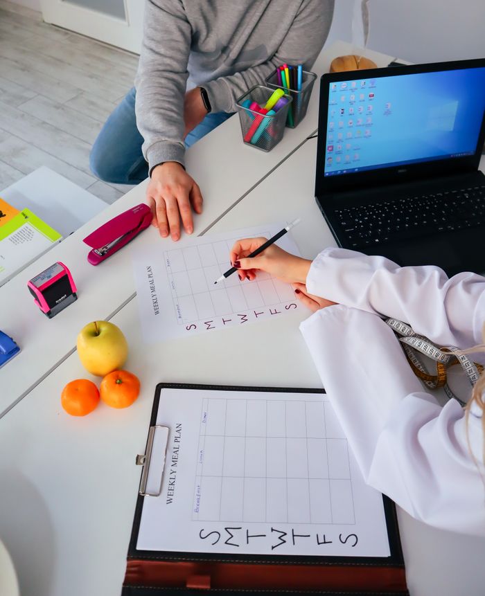 about-01 A nutritionist and a patient discuss a weekly meal plan in a modern office setting.