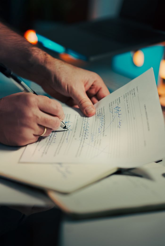 mission-02 Close-up of hands signing a business contract in an office environment. Ideal for legal and finance themes.